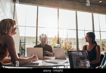 Young students sitting around a table in a library with books and laptop. university students doing group study in library. Stock Photo