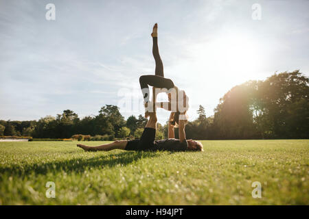 Healthy young couple doing acroyoga in park. Fit young man and woman doing various yoga poses in pair outdoors. Stock Photo