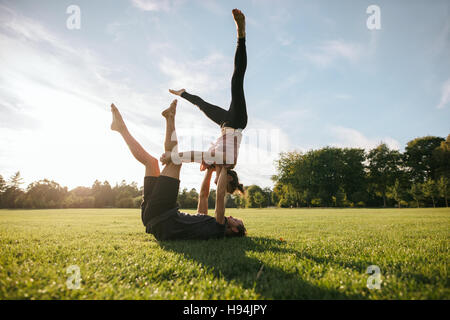 Strong and flexible young couple doing acrobatic workout. Man and woman in park practising pair yoga in morning. Stock Photo