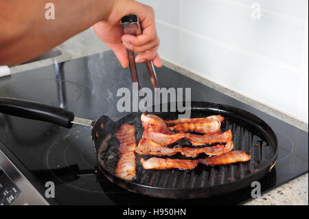 African American man cooking bacon on stove with a grill pan Stock Photo