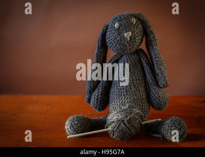 Handmade crocheted rabbit with a ball of yarn and crochet hook on a wooden table. Stock Photo
