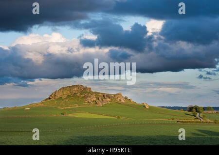 View of Almscliffe Crag hill lit by sun (gritstone tor, green fields separated by stone walls, beautiful hilly scenery) - North Yorkshire, England UK. Stock Photo