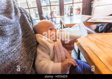 mother bottle feeding 5 month old baby girl in restaurant Stock Photo
