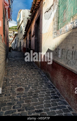 Steep, narrow, cobbled alleyway in Camara de Lobos in Madeira with terraces and banana plantations in the distance Stock Photo