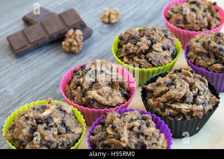 Fruit muffins on a yellow napkin and a grey wooden table. Walnuts and chocolate in the background. Stock Photo