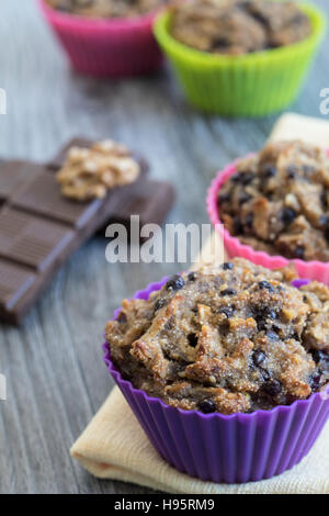 Fruit muffins on a yellow napkin and a grey wooden table. Walnuts, chocolate and two out of focus muffins in the background. Stock Photo