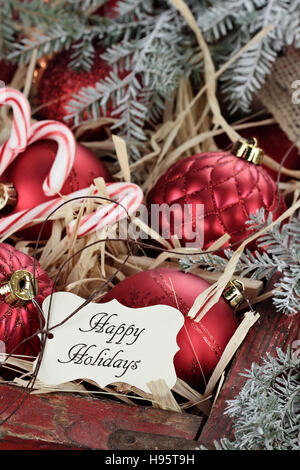 Christmas tag over glass Christmas ornaments and candy canes packed in an old antique wooden box with snow covered pine boughs s Stock Photo