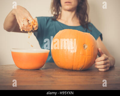 A young woman is sitting at a table and is picking the seeds out of a pumpkin Stock Photo