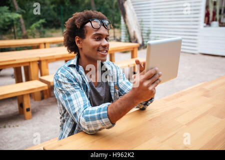Cheerful african young man sitting and using tablet outdoors Stock Photo