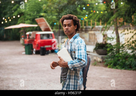Attractive african young man with backpack and books walking in the park Stock Photo