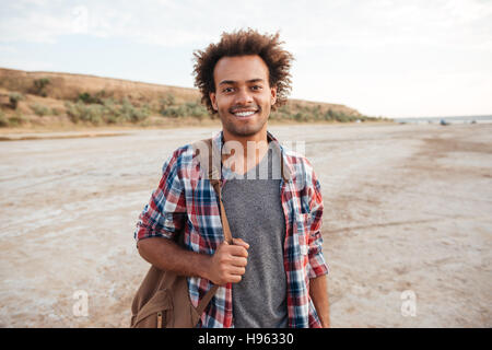 Cheerful attractive african young man standing outdoors and holding backpack Stock Photo