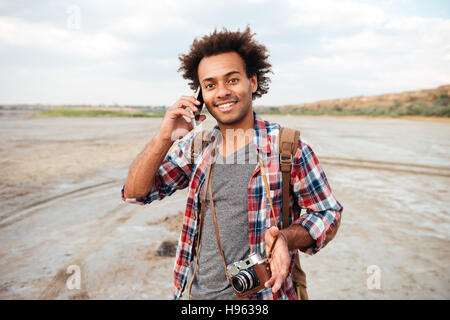 Happy african young man with vintage photo camera talking on mobile phone outdoors Stock Photo