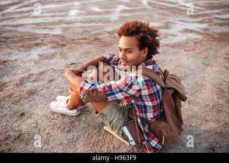 Handsome thoughtful african young man with backpack sitting and thinking Stock Photo