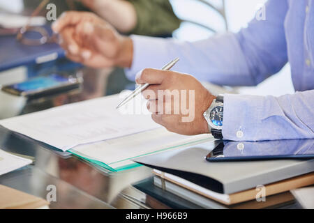 Businessman holding pen over paperwork in meeting Stock Photo