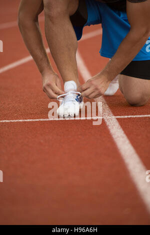 Young Man Runner tying his shoes on a running track. Shoelaces, Urban jogger Stock Photo