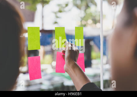 young businesswoman with colleague sticking adhesive notes on window in office Stock Photo