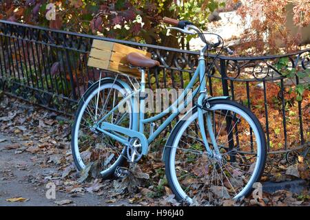 A Retro Light Blue Bicycle leaning against a wrought iron fence among fall foliage in Boston's Back Bay neighborhood. Stock Photo