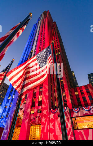 Rockefeller Center at twilight illuminated in white, red and blue. American flags flap in the wind. Midtown Manhattan, New York