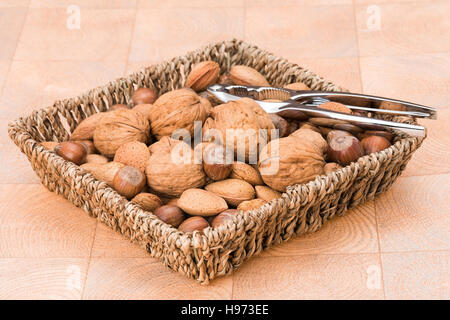A basket containing an assortment of nuts in their shells with a nut cracker Stock Photo