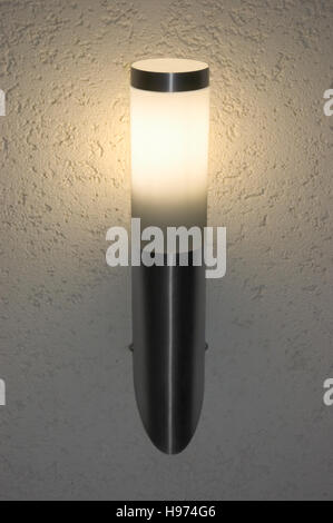 Bright glowing lit inox outdoor wall mounted torch lantern, large detailed vertical sconce closeup, grey textured stucco plaster pattern background Stock Photo
