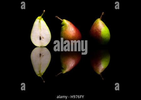 One cut in half and two whole red and green pears isolated on black reflective background Stock Photo