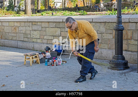 A shoeshine man cleans the area around his stand with an old fashioned straw broom. In Union Square Park in New York City. Stock Photo