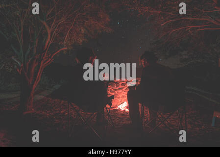 Couple sitting at burning camp fire in the night. Camping in the forest under starry sky, Namibia, Africa. Summer adventures and exploration in the af Stock Photo