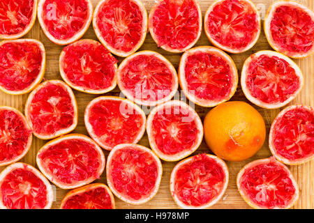 Overhead view of Squeezed Delicious ruby red grapefruit halves by glass against a wooden background one with downright position Stock Photo