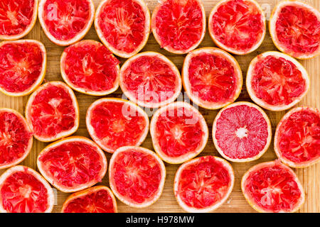 Background pattern of fresh squeezed ruby grapefruit halves arranged side by side on a bamboo cutting board viewed from above with one unsqueezed one Stock Photo