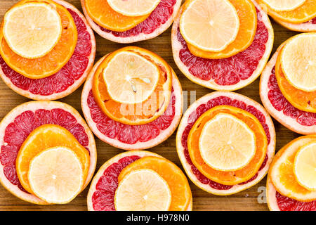 High Angle Full Frame Still Life View of Sliced Ruby Red Grapefruit Stacked with Ripe Orange and Lemon Slices on Rustic Wooden Cutting Board Stock Photo