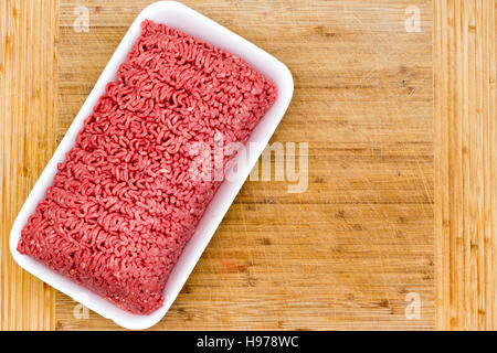 Punnet of fresh raw ground beef on a bamboo cutting board ready to be used in the kitchen as a cooking ingredient, overhead view Stock Photo