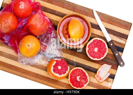 High Angle Still Life of Whole and Sliced Ruby Red Grapefruit Citrus on Wooden Cutting Board with Sharp Knife on White Background Stock Photo