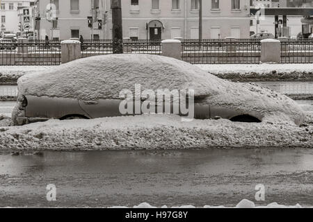 Car on winter road covered with snow side view. Vehicle on snowy alley in the morning after snowfall in city. A street with car covered with snow in wintertime. Stock Photo