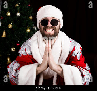 bad rastoman Santa Claus smiles and making hands sign namaste on the background of Christmas tree Stock Photo