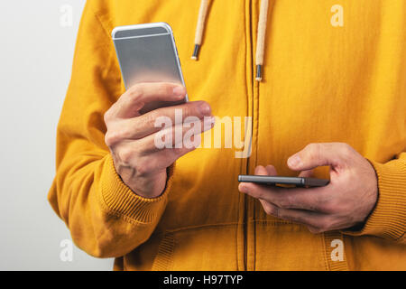 Man using two mobile phones for SMS communication, male person wearing yellow shirt with zipper sending text messages from dual smartphone devices Stock Photo