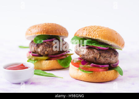 Big sandwich - hamburger burger with beef, pickles, tomato and red onions on a light background. Stock Photo