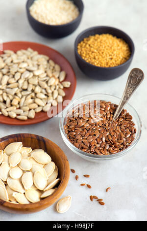 Assorted oil seeds (flax, sesame, pumpkin, sunflower, mustard) in small bowls on stone background - organic ingredients for healthy vegetarian vegan n Stock Photo