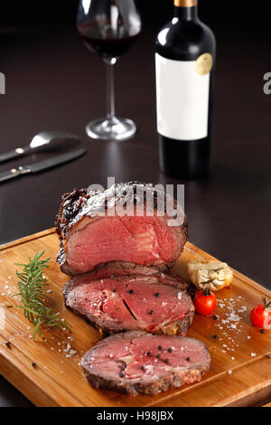 Grilled rib eye steak sliced on a cutting board with a bottle of red wine Stock Photo