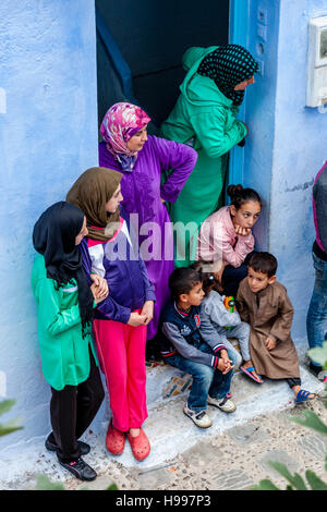 A Moroccan Family Watching The Life In Their Street From Their Front Door, Chefchaouen, Morocco Stock Photo