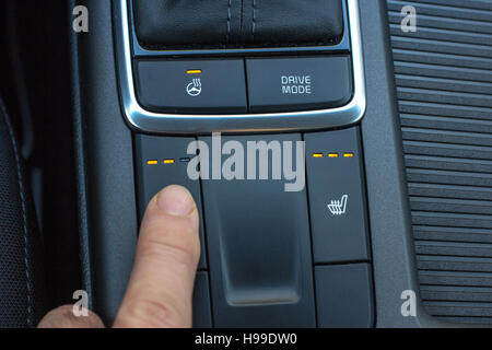 Finger on seat and steering heating controls. Close up shot of modern car central console. Stock Photo