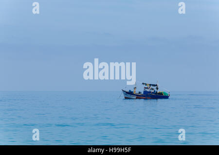 Blue painted small fishing boat in front of the Angolan coast of the Namib Desert. Dominating blue colors and calm mood. Stock Photo