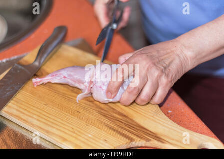 Senior woman hands cutting raw rabbit meat on a wodden table. Shallow dof, selective focus on woman hand. Stock Photo