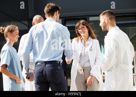 Female Doctor shaking hands with businessman outdoors Stock Photo