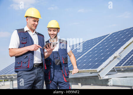 Construction workers next to solar panels looking at digital tablet Stock Photo