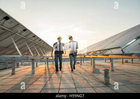 Construction workers with blueprint on roof of solar power station Stock Photo