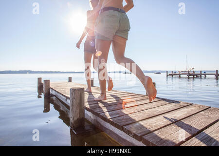 Two young women running on pier by lake Stock Photo