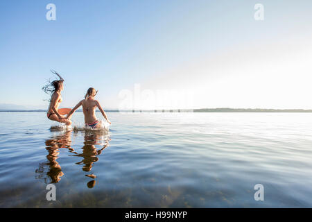 Two young women jumping into lake Stock Photo