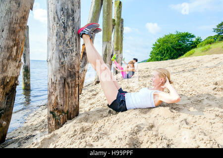 Young women on beach doing sit-ups Stock Photo