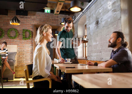 Waiter serving espresso to guests in restaurant Stock Photo