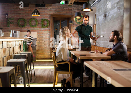 Waiter serving espresso to guests in restaurant Stock Photo